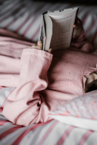 Mädchen mit rosa Kleid und Buch in Bett
